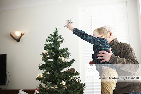 Senior man lifting grandson to place star on christmas tree
