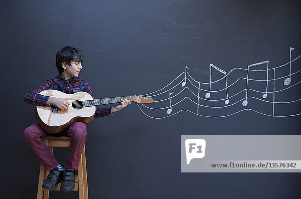 Junge spielt Gitarre vor einer Tafelwand mit Musiknotation