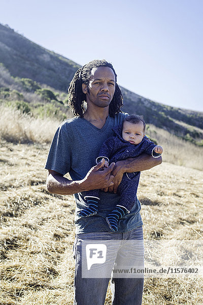 Portrait of mature man standing on beach  holding baby boy