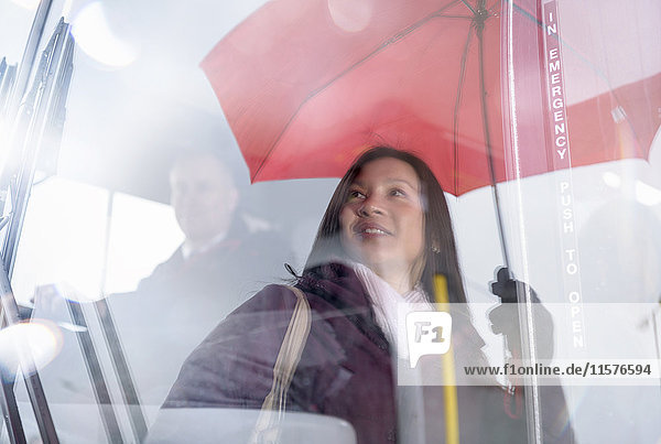 Fahrgast mit Regenschirm spiegelt sich in der Windschutzscheibe eines Elektrobusses