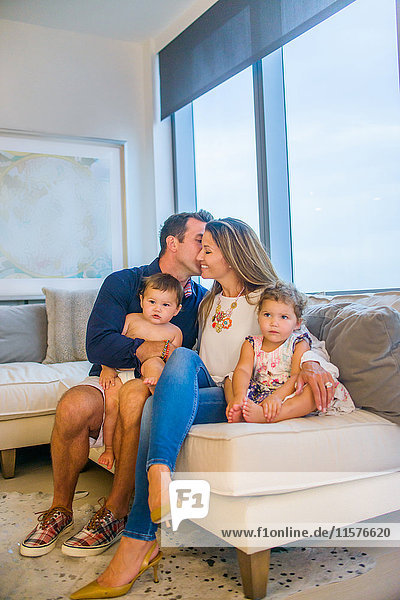 Porträt einer jungen Familie auf dem Sofa sitzend  Mutter und Vater küssen sich