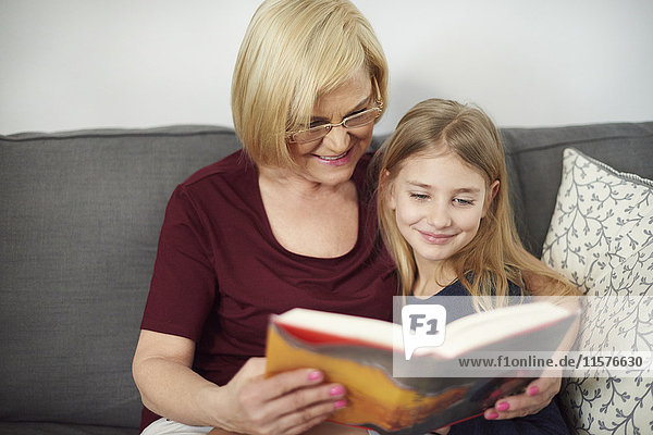 Großmutter und Enkelin lesen Buch auf Sofa