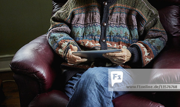 Ältere Frau auf Stuhl sitzend,  hält digitales Tablet,  Mittelteil