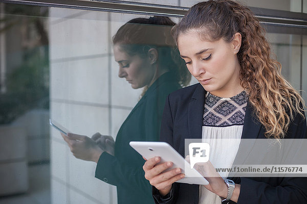 Junge Geschäftsfrau  im Freien stehend  am Fenster  mit digitalem Tablett