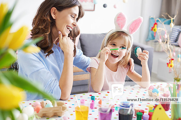 Woman and daughter painting easter eggs at table