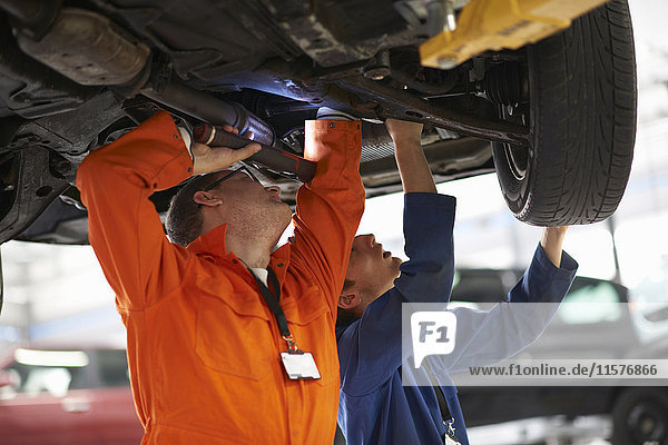 College-Studenten der Fachrichtung Mechanik inspizieren Fahrzeugunterseite in Reparaturwerkstatt