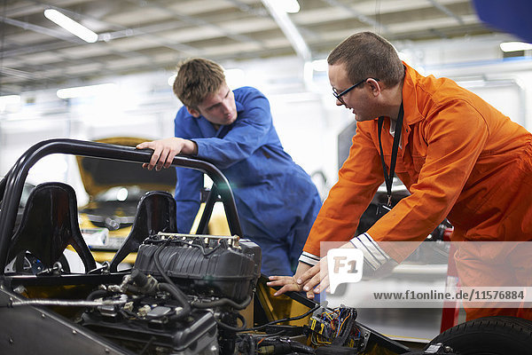 College mechanic students discussing racing car engine in repair garage