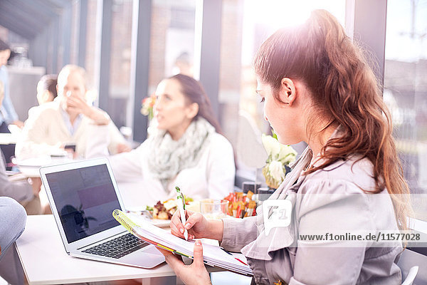 Businesswoman making notes during working lunch in restaurant