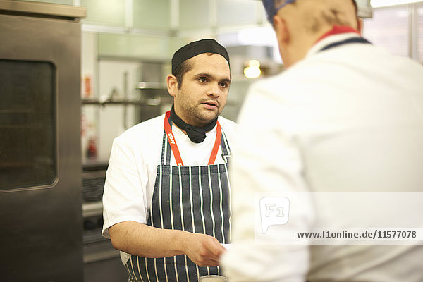 Chef lecturer explaining recipe to teenage catering student in college kitchen
