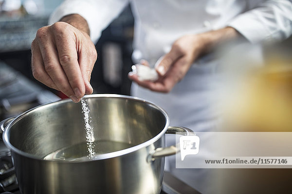 Chef putting salt in pan of water on stove  close-up