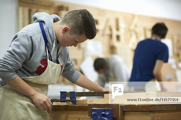 Männlicher Teenager-Schreinerei-Student beim Justieren einer Holzklemme in einer College-Werkstatt