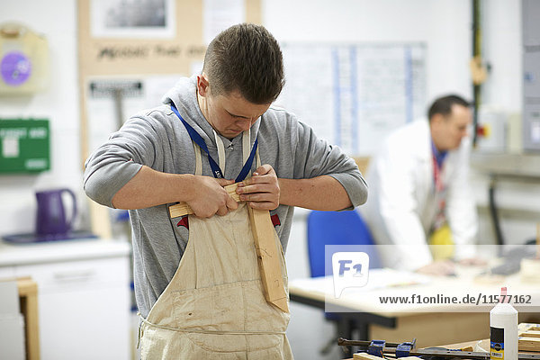 Male teenage carpentry student pushing wood joints together in college workshop