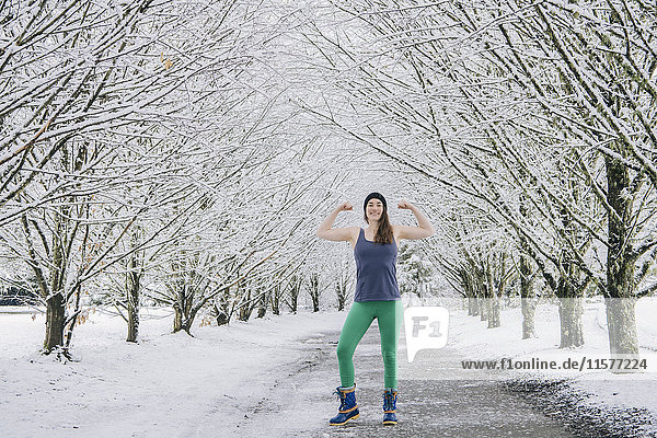 Porträt einer Frau  die ihre Muskeln spielen lässt  in schneebedeckter ländlicher Landschaft