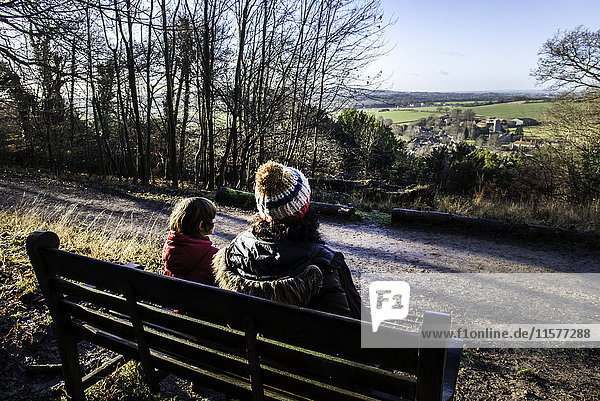 Mother and son sitting on bench in rural setting  looking at view  rear view