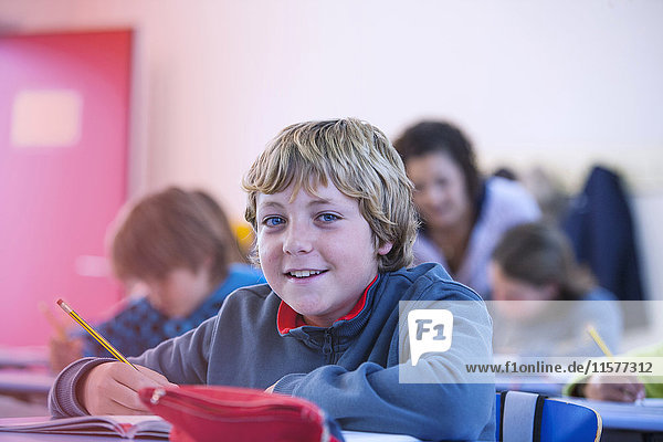 Porträt eines Jungen im Klassenzimmer  der am Schreibtisch sitzt und lächelt
