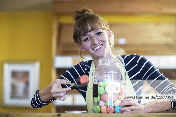 Porträt einer jungen Frau im Lebensmittelgeschäft  die süße Speisen aus dem Glas nimmt