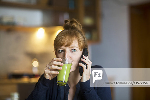 Junge Frau trinkt Smoothie  mit Smartphone