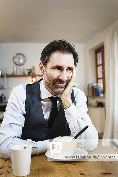 Smiling mature man with chin on hand at breakfast in kitchen