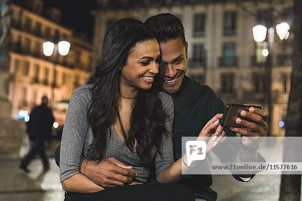 Couple in city at night looking at smartphone Lisbon Portugal