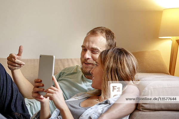 Mittelgroßes erwachsenes Paar entspannt sich auf dem Sofa und schaut auf ein digitales Tablett