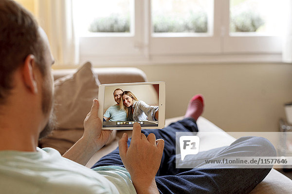 Mann sitzt auf dem Sofa und betrachtet Fotos auf einem digitalen Tablet  Rückansicht