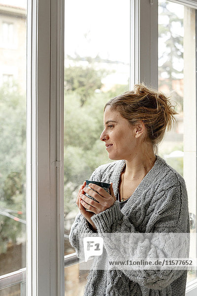 Woman at home  looking out of window  holding hot drink