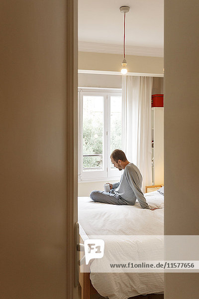 Man at home  sitting on bed  holding hot drink