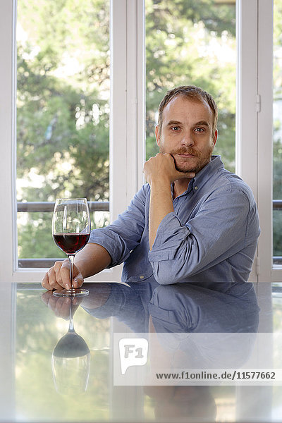 Man at home  sitting at table  holding glass of wine  pensive expression