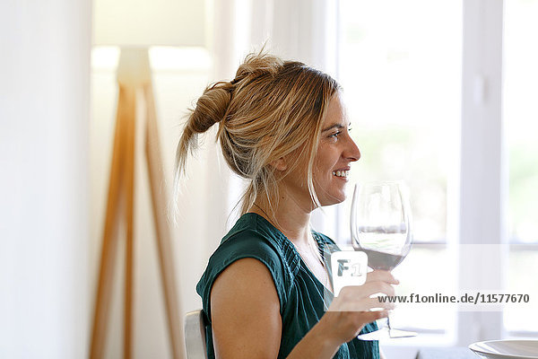 Frau zu Hause  hält ein Glas Wein in der Hand und lächelt