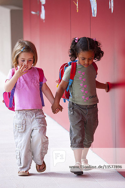 Zwei Mädchen im Vorschulalter halten sich an den Händen und gehen vor der Vorschule