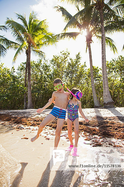 Two children fooling around on beach  wearing swimwear and snorkels