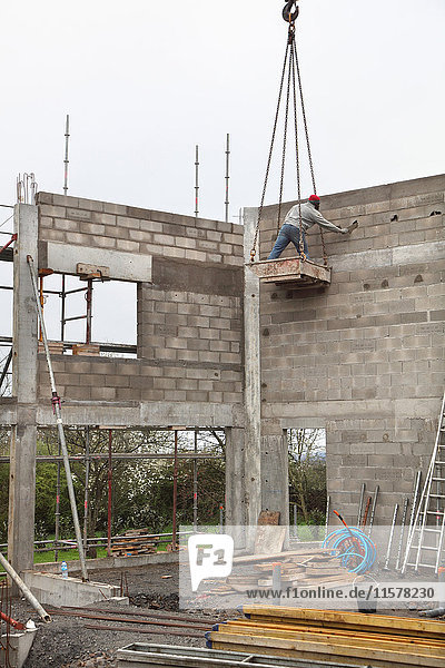 Frankreich  Hausbau  Erhöhung der Hausmauern. Sicherheitsproblem bei der Handhabung durch Baumaschinen. Verletzung der Sicherheit : Maurer im Eimer ohne Helm