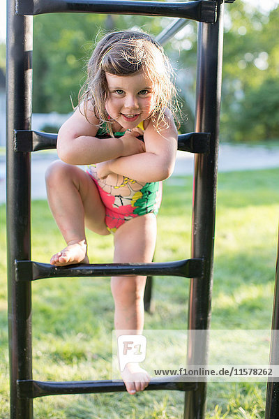 Porträt eines Mädchens in Badebekleidung auf einem Klettergerüst im Garten stehend