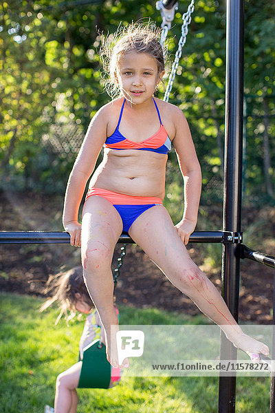 Porträt eines Mädchens im Bikini das auf einem Klettergerüst im Garten sitzt