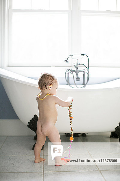 Rear view of naked male toddler playing with beads in bathroom