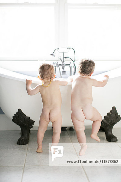 Rear view of male and female toddlers looking into bathtub