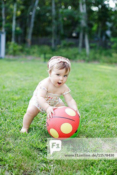 Barefoot female toddler picking up spotty ball in garden