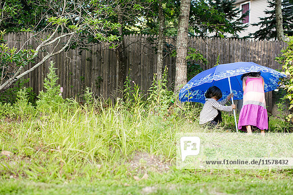 Junge und Mädchen stellen Sonnenschirm im Garten auf