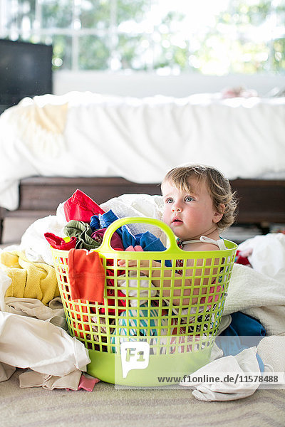 Female toddler sitting in basket amongst laundry