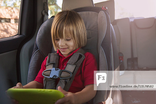 Mädchen im Auto-Sicherheitssitz betrachtet digitales Tablet