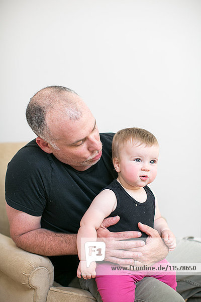 Reifer Mann auf Sessel sitzend mit kleiner Tochter auf dem Knie
