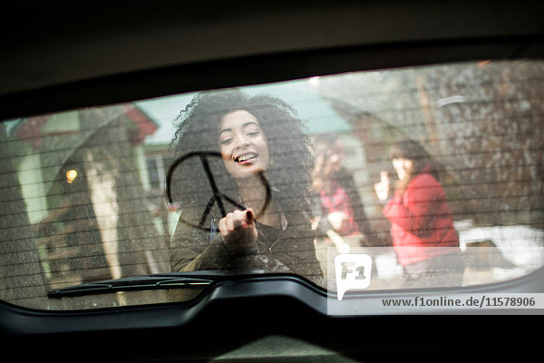 Junge Frau zeichnet Friedenszeichen am Fenster des Autos  Blick durchs Fenster