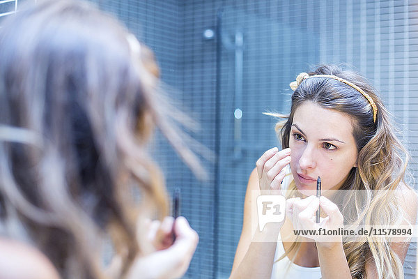 Reflexion einer jungen Frau im Spiegel beim Schminken