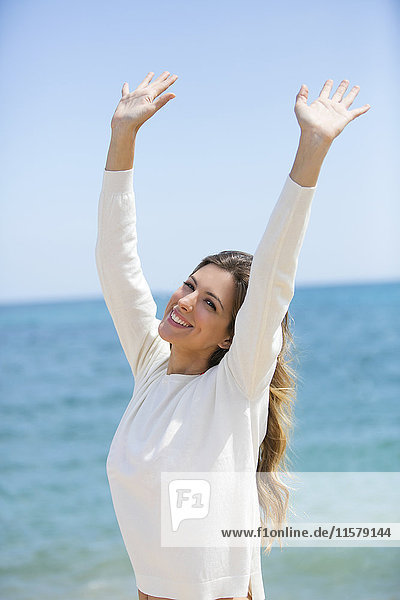 Hübsche,  fröhliche Frau mit den Händen am Strand,  die vor der Kamera lächelt.