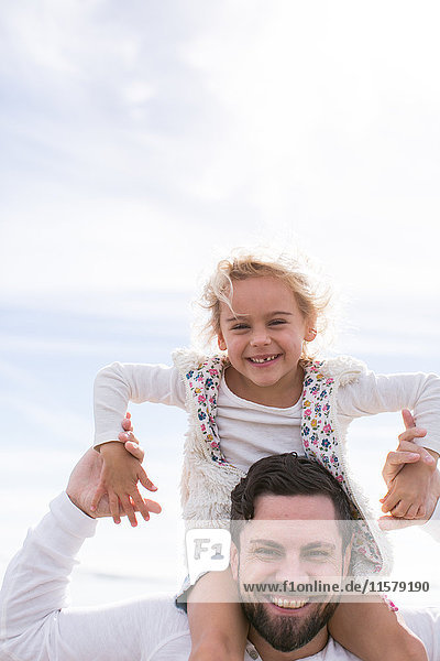 Portrait of mature man giving daughter a shoulder carry at coast