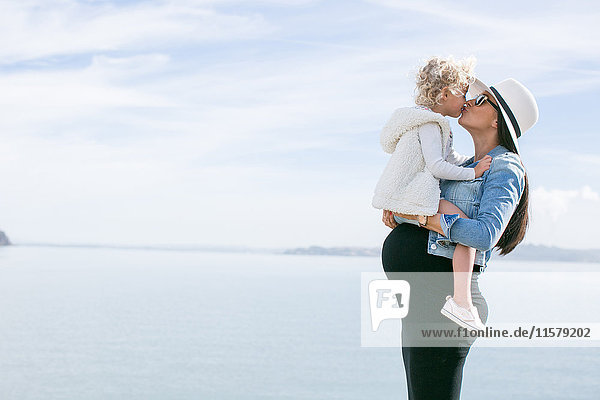 Schwangere Mutter küsst Tochter an der Küste