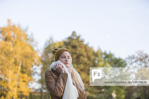 Porträt einer hübschen blonden Frau mit Haube und Schal im Herbst mit geschlossenen Augen