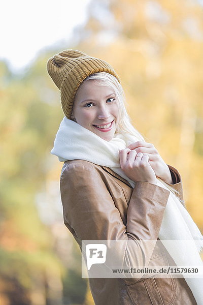 Porträt einer zufriedenen hübschen blonden Frau mit Haube und Schal im Herbst lächelnd vor der Kamera