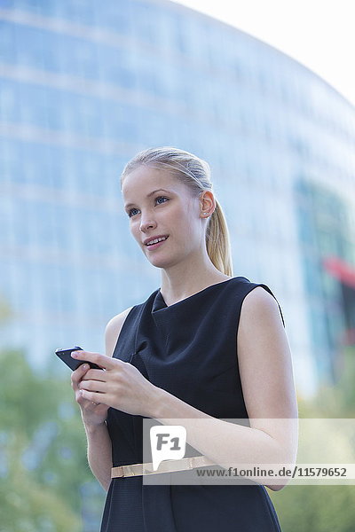Hübsche elegante Frau  die ihr Handy vor einem Bürogebäude in der Innenstadt überprüft.