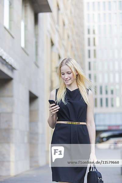 Hübsche elegante Frau  die ihr Handy vor einem Bürogebäude in der Innenstadt überprüft.